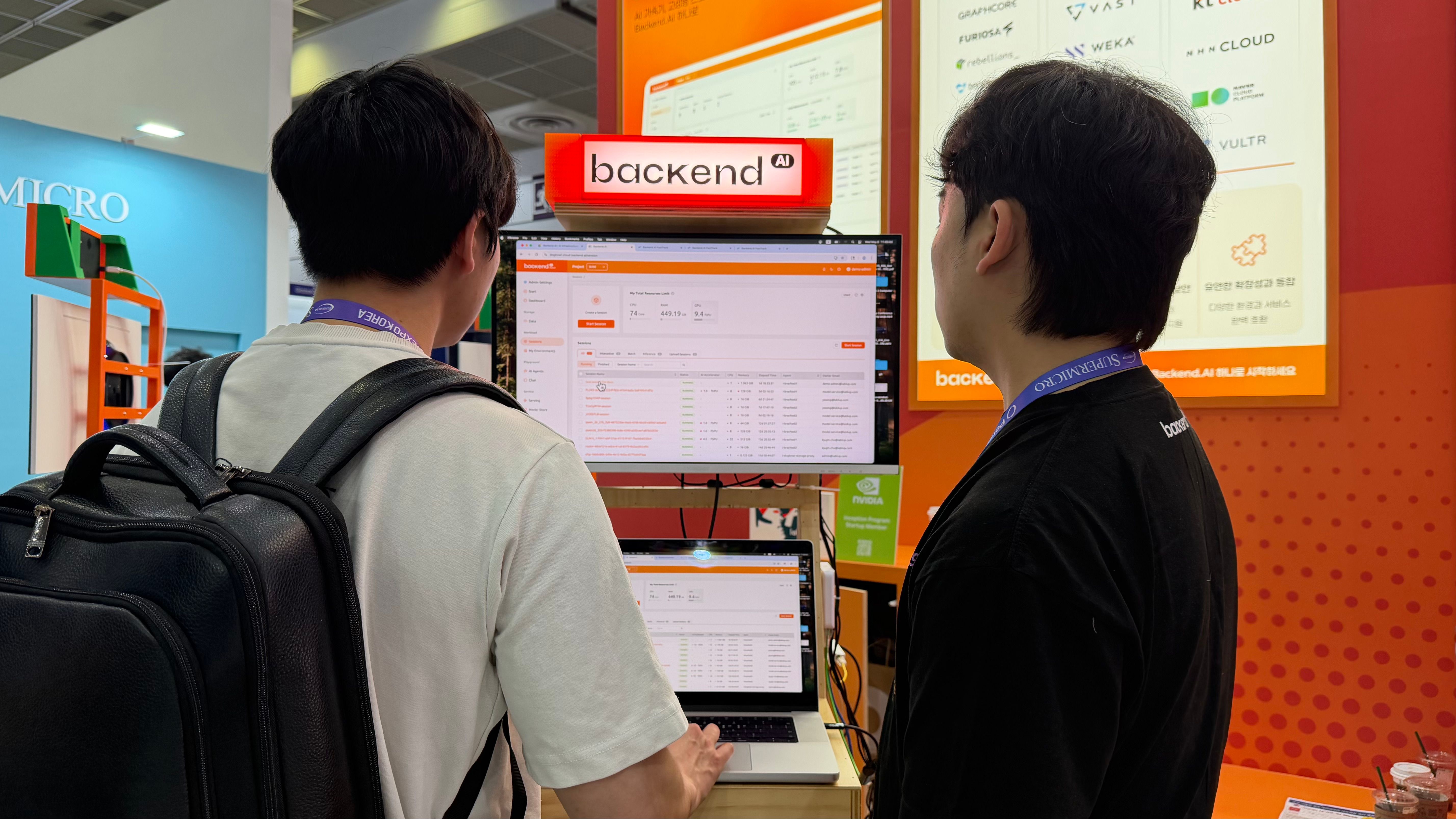 Two visitors looking at a Backend.AI monitor during a booth demo.